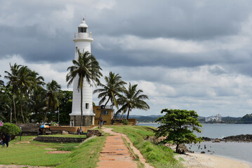 Galle Lighthouse before rain, Sri Lanka. Amazing white tower in Galle port. Pre-storm clouds usual for Ceylon landscape. Palm trees surround Galle Beacon creating unique exotic mood for visitors.