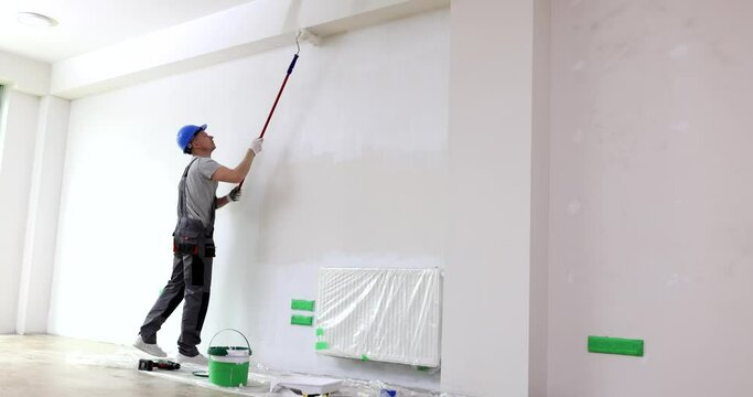 Man paints ceiling with roller in white room. Wall and ceiling repair and painting