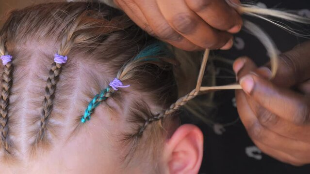 The hands of an African woman are braiding the braids of a little girl close up view.