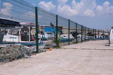 Boats docked in the small harbor, sheltered in the bright blue sky with white scattered clouds, behind green fence