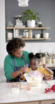 Vertical video of african american mother and daughter preparing dough in kitchen, slow motion