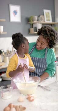 Vertical video of african american mother and daughter preparing dough in kitchen, slow motion