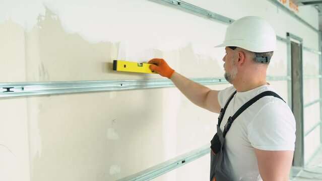 A man builder measures of the horizontal deviation of plasterboard wall