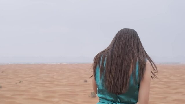 Young woman with dark hair in a long blue dress standing on the sand of the desert
