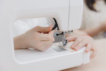 Closeup hand of Little girl learns to sew, working with modern sewing machine on seamstress master class in school