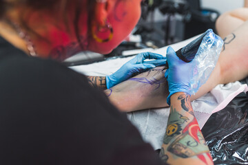 Leg with a pattern and black paint. New tattoo on leg. Tattooing master working in blue sterile gloves. High quality photo