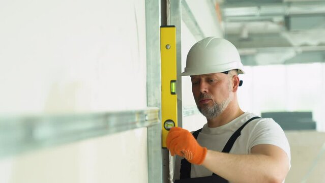 A man builder measures of the vertical deviation of plasterboard wall. Bubble level ruler