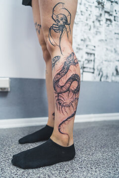 Dragon tattoo concept. Legs of a caucasian person covered with black ink tattoos. New tattoo at leg area. Skin irritation. High quality photo