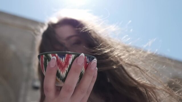 A young woman with long hair holding a painted ceramic tea cup with an Uzbek ornament in her hands