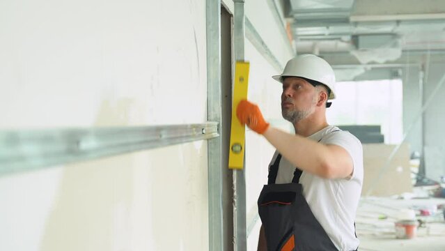 A man builder measures of the vertical deviation of plasterboard wall. Bubble level ruler
