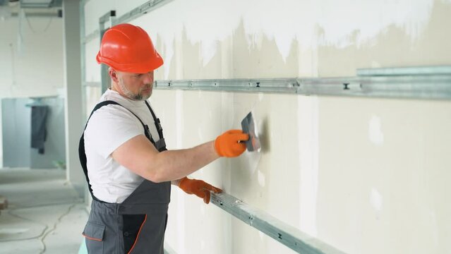 Finishing and Patching Drywall Walls by Caucasian Remodeler in His 45s. Construction Industry