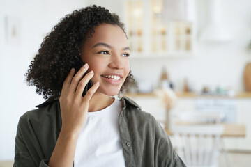 Smiling girl enjoys pleasant phone call at home. Biracial teen gets good news, chats happily on...