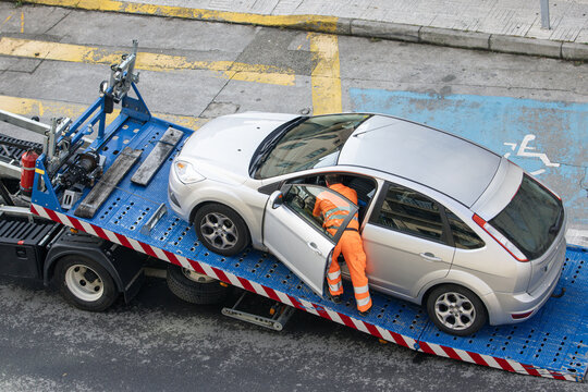 Damaged car being loaded onto tow truck by a worker. Towing service on the city. Roadside assistance concept