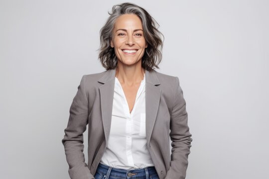 Portrait Of A Smiling Mature Businesswoman Standing With Hands In Pockets Over Gray Background