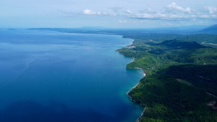 Aerial view of a tropical island. Blue sea, sandy beach, jungle and white clouds over the horizon.