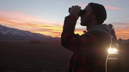 Man with binoculars near car looking through binocular searching for animal. Male hiker learning with nature while traveling with car in mountain landscape. - Powered by Adobe