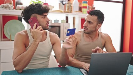 Two men couple shopping with laptop and credit card talking on smartphone at dinning room - Powered by Adobe