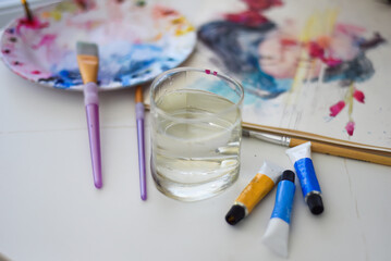 paint brushes and water on a table with and palette for art