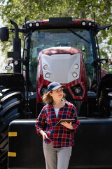Woman farmer with a digital tablet on the background of an agricultural tractor.
