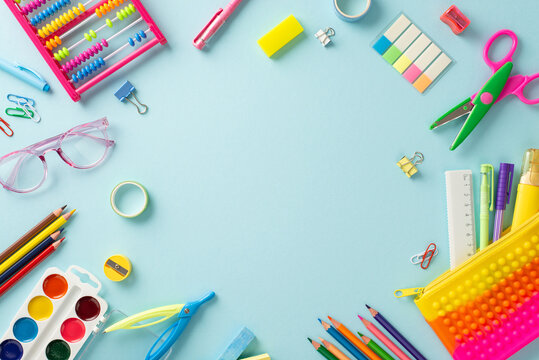 Immerse yourself in the world of early education with this captivating top-down image: an array of vibrant school supplies on a pastel blue backdrop, offering ample round frame for text or advertising