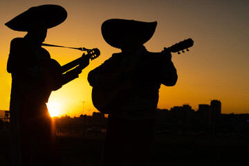 Silhouettes of a mexican musicians mariachi band on a background of city panorama..