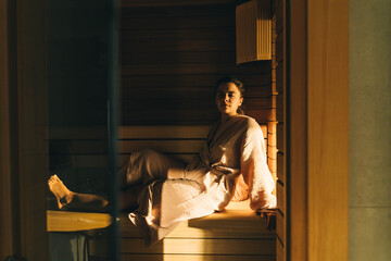 Obraz na płótnie Canvas Tanned young woman is sitting in sauna.