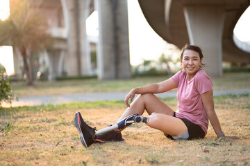 Portrait Happy Asia woman with prosthetic leg and sitting on grass in the park