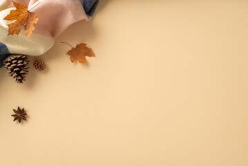 Embrace the cozy fall atmosphere at home: High angle view photo featuring a warm patchy scarf, maple leaves and empty space for text or adverts on a beige isolated background