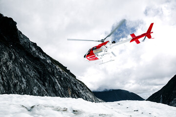 Fototapeta na wymiar White and red rescue helicopter saving people from a glacier in the mountains