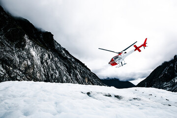 White and red rescue helicopter saving people from a glacier in the mountains