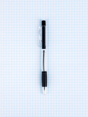 Close-up of a black ballpoint pen lying on a checkered notebook, ready to start work