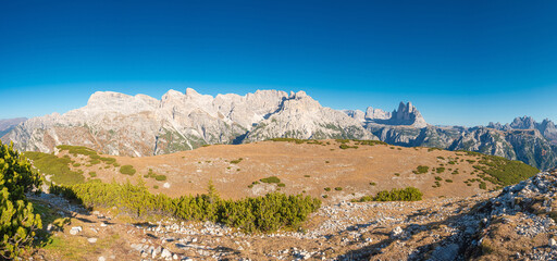 Panoramic over beautiful magical Three Dolomite peaks at the national park Three Peaks, Tre Cime Drei Zinnen in Autumn colors at blue sky and sunny day, South Tyrol, Italy