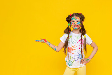 A child smeared with paint. A little girl, painted with multicolored paints, holds your advertisement in the palm of her hand. Children's creativity. Yellow isolated background. Copy space. Banner.
