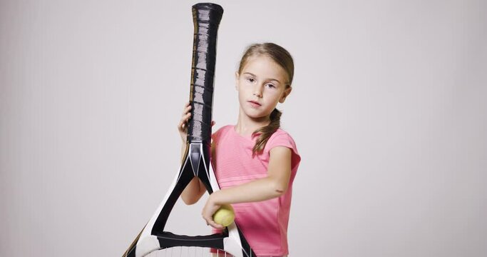 Young female tennis player with big oversize racket. Girl posing in pink sports outfit and bouncing a ball with her hand.