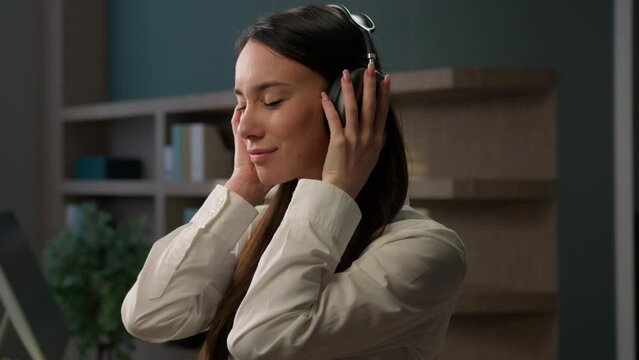 Relaxed Caucasian woman in workplace enjoying sound in wireless headphones close eyes inspired enjoy song calm tranquil businesswoman listen music in office work pause relax business girl song audio