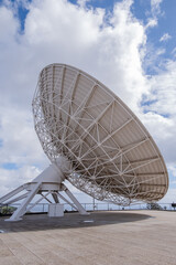 Side view of large satellite dish to observe the cosmos, with large white clouds in the background.