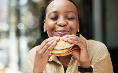 Fotobehang Restaurant, fast food and black woman eating a burger in an outdoor cafe as a lunch meal craving deal. Breakfast, sandwich and young female person or customer enjoying a tasty unhealthy snack © JessicaLeigh J/peopleimages.com