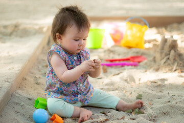 Adorable 9 months old baby playing outdoors - lifestyle portrait of mixed ethnicity Asian Caucasian baby girl playing with block toys happy and carefree at playground sitting on sand