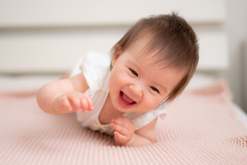lifestyle home portrait of 9 months old mixed ethnicity Asian Caucasian baby girl playing happy and carefree on bed crawling laughing and excited in childhood and nursery concept