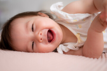 lifestyle home portrait of 9 months old mixed ethnicity Asian Caucasian baby girl playing happy and carefree on bed crawling laughing and excited in childhood and nursery concept