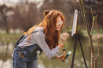 A woman is painting on a easel