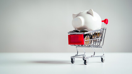 Piggy bank in shopping cart with plenty full of coins on white table background. Pig jar money...