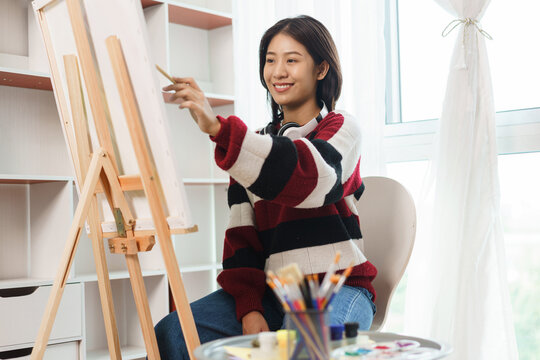 The art concept, Asian female artist in sweater use paint brush to painting on canvas in art studio