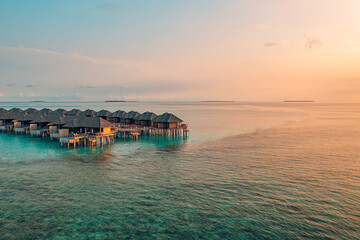 Sunset on Maldives island, luxury water villas resort and wooden pier. Beautiful aerial sky clouds...