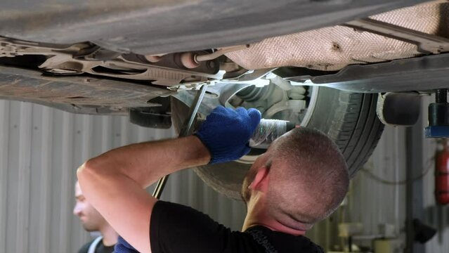 Auto mechanic working underneath car lifting machine at the garage. Auto repair shop, Car service, repair.
