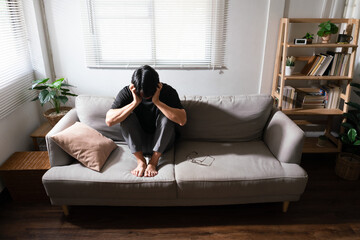 Man with mental health problem sitting on couch and use hands to covering ears from noise anything