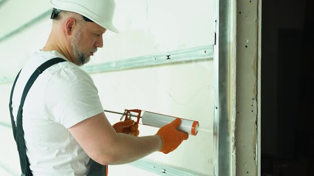 Worker in uniform is applying polyurethane foam to fill gap on drywall wall