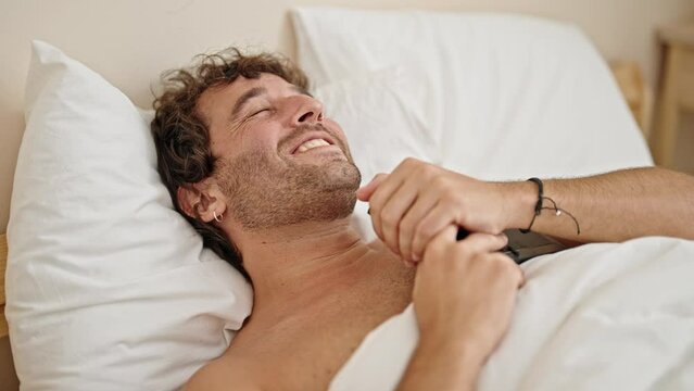 Young hispanic man lying on bed shirtless hugging photo at bedroom