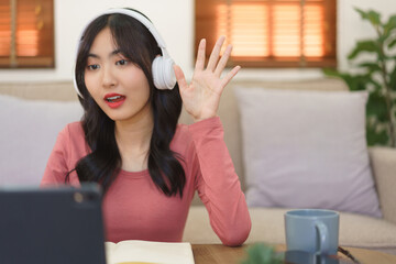 Young businesswoman greeting with partners and writing note in notebook while meeting on video call