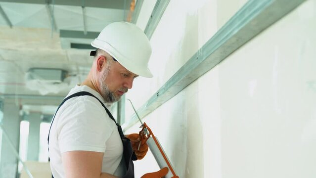 Worker in uniform is applying polyurethane foam to fill gap on drywall wall